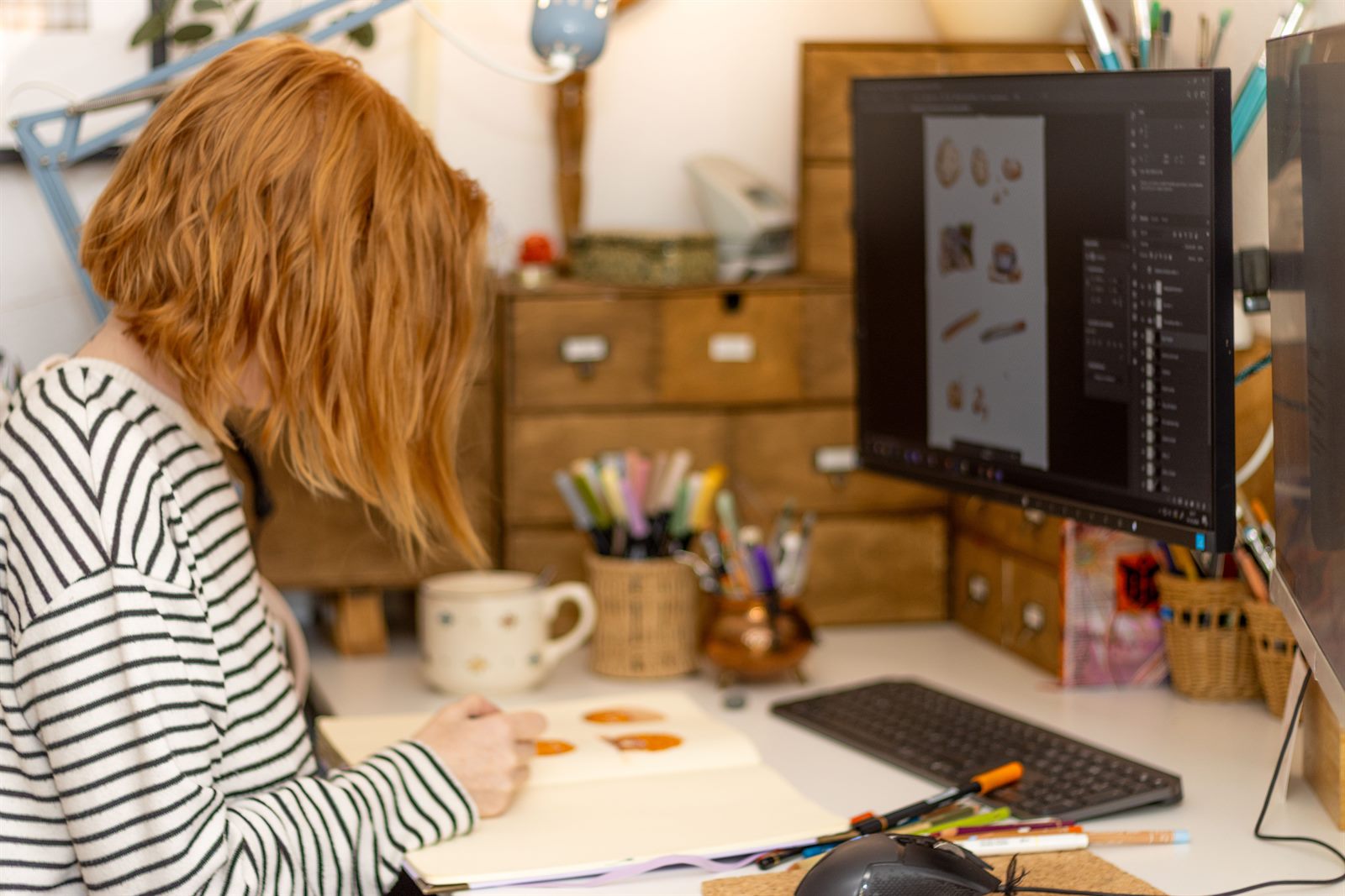 Nadine zeichnet am Schreibtisch, daneben der Monitor mit Illustrationen